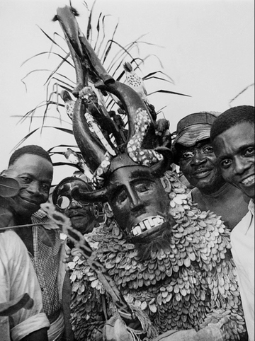 A black and white photograph of a person in a masquerade outfit surrounded by other people.