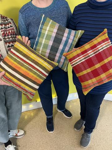 Three people with their faces out of shot holding colourful woven cushions