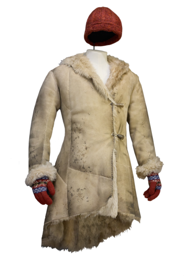 A tanned hide coat on a mannequin with red knitted gloves poking out from the sleeves and a red knitted hat suspended above.
