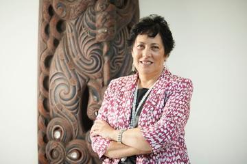 Portrait of a smiling woman standing in front of a Māori carving