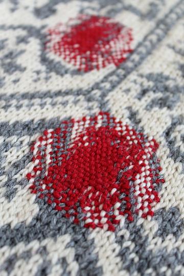 Red woollen darn on grey and white knitted garment