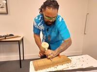 Robbie Atatoa, Mangaian carver and knowledge holder, carving a small block of wood in the Pitt Rivers Museum lecture theatre