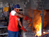 A man uses metal tongs to reach into a fire in a red brick waist-height fireplace.