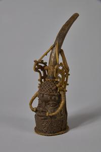 Figurine of a head with intricate ornaments and a large tusk emerging from the top, made from beeswax
